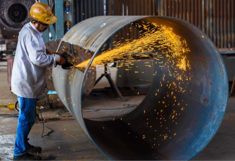 man cutting hole in metal cylinder